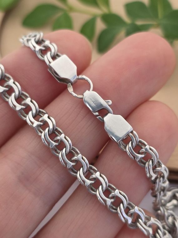 Närbild på ett bismarckhalsband i silver som hålls i en hand.